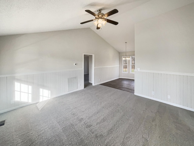 unfurnished living room featuring lofted ceiling, dark carpet, ceiling fan with notable chandelier, and a textured ceiling