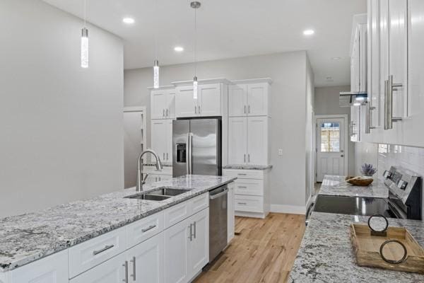 kitchen with light wood finished floors, pendant lighting, appliances with stainless steel finishes, white cabinetry, and a sink