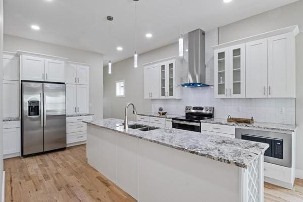 kitchen with a sink, appliances with stainless steel finishes, white cabinets, and wall chimney range hood