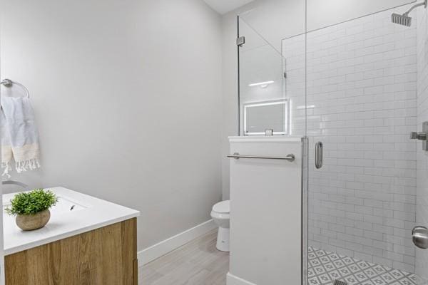 bathroom featuring baseboards, toilet, a stall shower, wood finished floors, and vanity