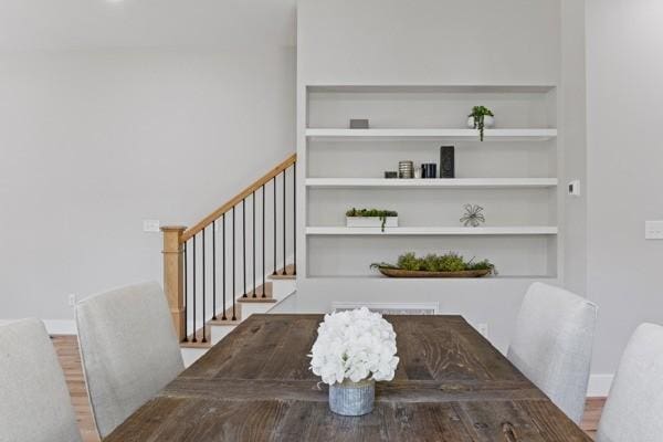 dining area with baseboards, built in shelves, wood finished floors, and stairs