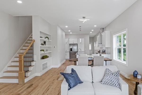 living room featuring built in shelves, baseboards, light wood-type flooring, stairs, and recessed lighting