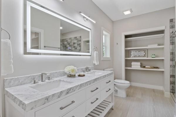 full bath with a sink, tiled shower, toilet, and double vanity