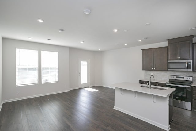 kitchen with sink, dark wood-type flooring, stainless steel appliances, and a center island with sink