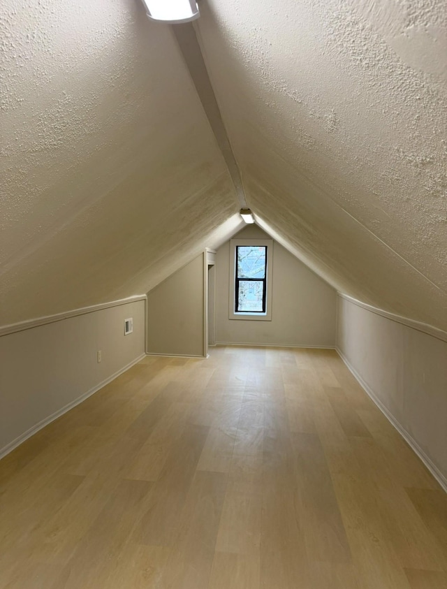 additional living space featuring vaulted ceiling, a textured ceiling, and light wood-type flooring