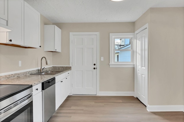 kitchen with sink, light hardwood / wood-style flooring, appliances with stainless steel finishes, white cabinetry, and a textured ceiling