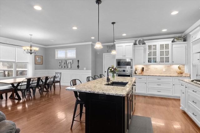 kitchen with appliances with stainless steel finishes, white cabinetry, ornamental molding, an island with sink, and decorative light fixtures