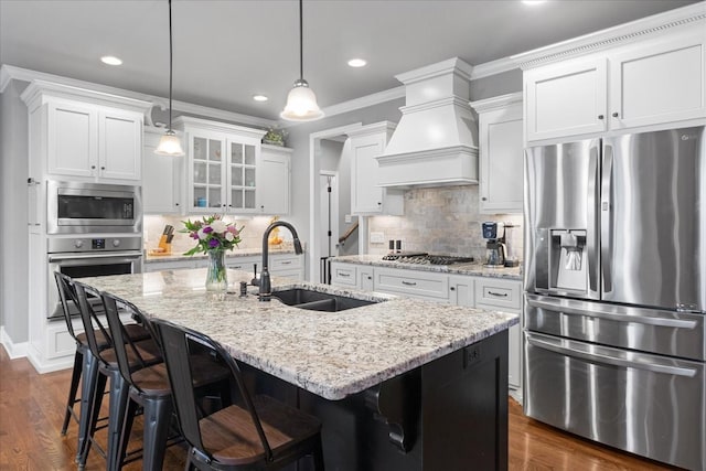 kitchen featuring sink, custom exhaust hood, ornamental molding, stainless steel appliances, and a kitchen island with sink