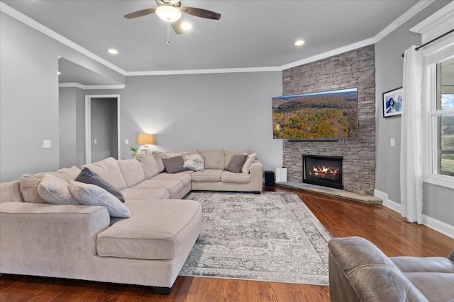 living room with wood-type flooring, a stone fireplace, ceiling fan, and crown molding