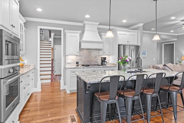 kitchen featuring a center island with sink, custom range hood, white cabinets, and appliances with stainless steel finishes