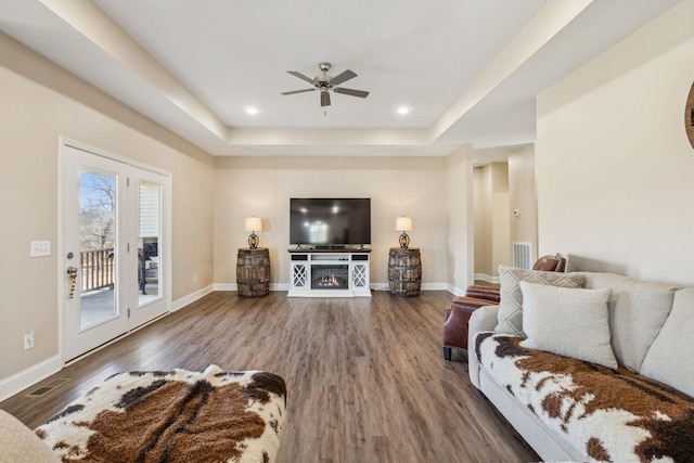 living room with dark hardwood / wood-style floors, a raised ceiling, and ceiling fan