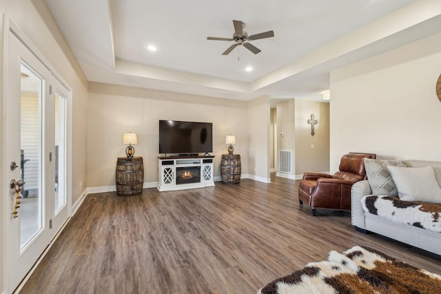 living room featuring a healthy amount of sunlight, dark hardwood / wood-style floors, ceiling fan, and a tray ceiling