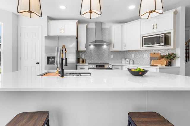 kitchen featuring stainless steel appliances, a kitchen breakfast bar, hanging light fixtures, and wall chimney range hood