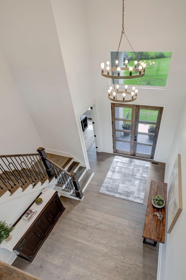 foyer entrance featuring hardwood / wood-style flooring, french doors, a chandelier, and a towering ceiling