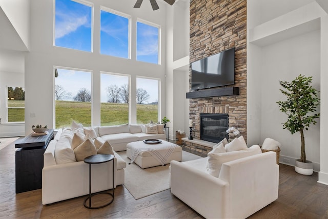 living room featuring hardwood / wood-style flooring, a stone fireplace, a high ceiling, and ceiling fan