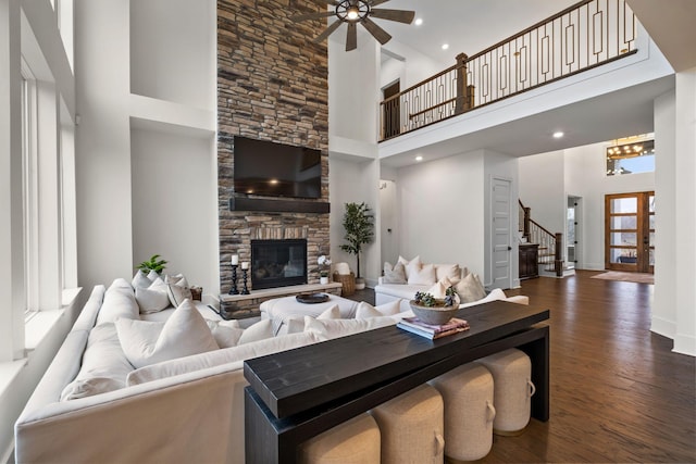 living room featuring ceiling fan, a towering ceiling, a fireplace, and dark hardwood / wood-style flooring