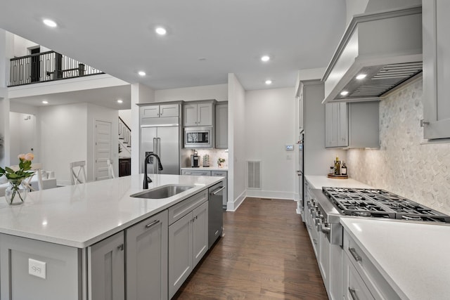 kitchen featuring a large island, sink, gray cabinets, built in appliances, and custom range hood