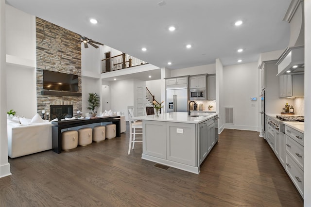 kitchen with a kitchen bar, custom exhaust hood, gray cabinetry, built in appliances, and a large island