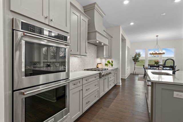 kitchen with dark wood-type flooring, sink, tasteful backsplash, custom range hood, and stainless steel appliances