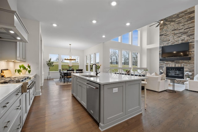 kitchen featuring premium range hood, an island with sink, sink, stainless steel dishwasher, and dark wood-type flooring