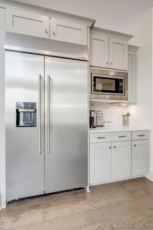 kitchen featuring tasteful backsplash, built in appliances, and light hardwood / wood-style flooring