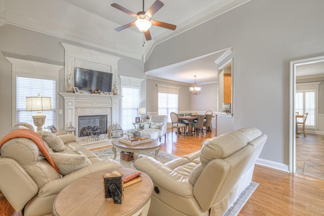 living room with ceiling fan with notable chandelier, ornamental molding, vaulted ceiling, and light hardwood / wood-style flooring