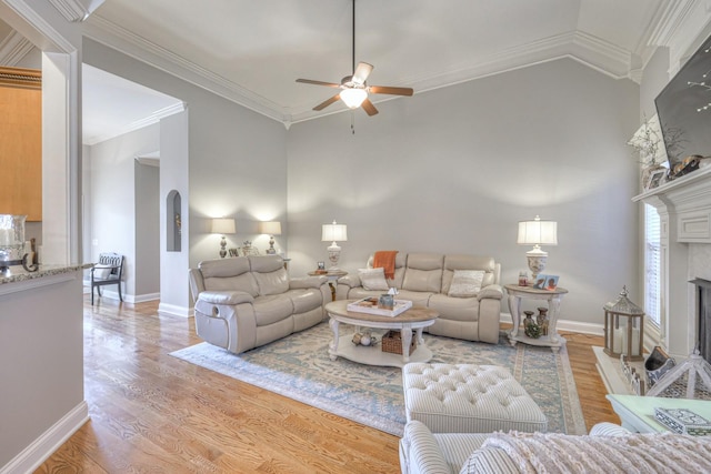 living room featuring vaulted ceiling, a tiled fireplace, ornamental molding, ceiling fan, and light hardwood / wood-style floors