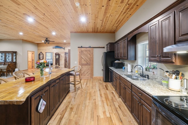 kitchen with wood counters, sink, wooden ceiling, a barn door, and light hardwood / wood-style floors