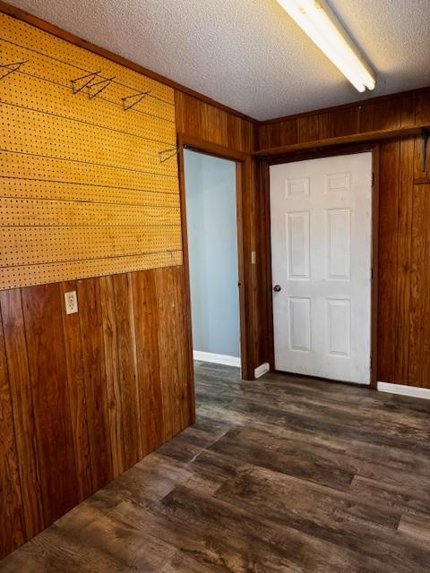 hall featuring dark wood-type flooring, wooden walls, and a textured ceiling