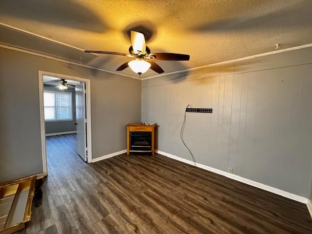 spare room featuring dark wood-type flooring, a textured ceiling, ornamental molding, wooden walls, and ceiling fan