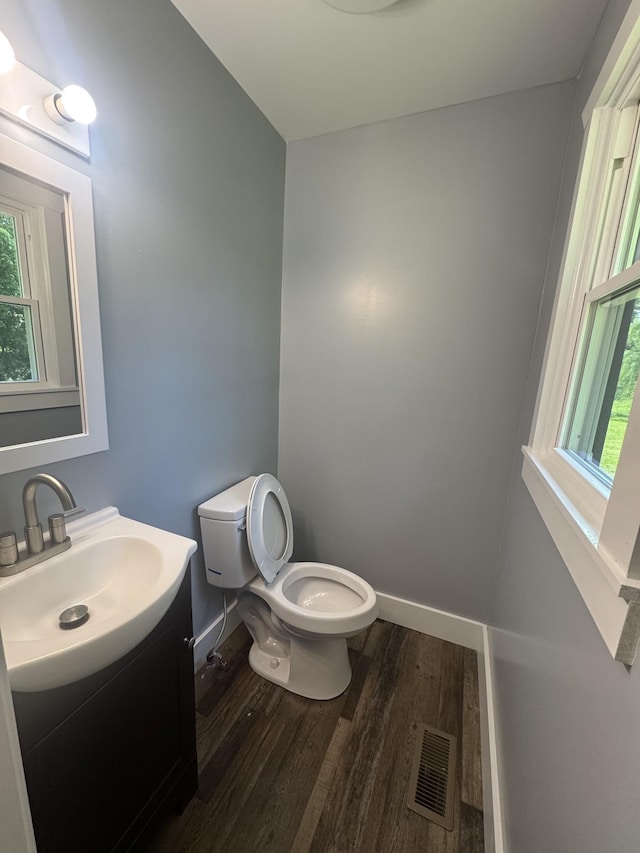 half bathroom featuring plenty of natural light, visible vents, wood finished floors, vanity, and toilet