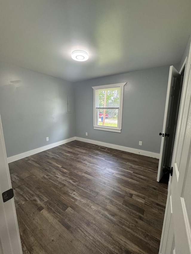 unfurnished room featuring baseboards and dark wood-type flooring