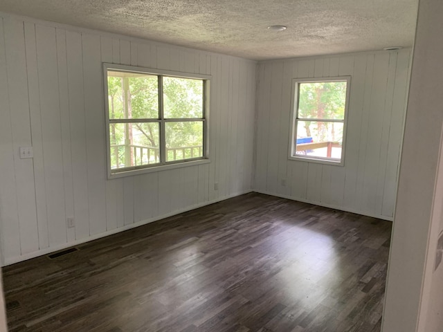 empty room with plenty of natural light, dark hardwood / wood-style floors, a textured ceiling, and wood walls