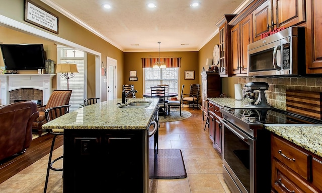 kitchen with light stone counters, appliances with stainless steel finishes, a kitchen bar, and a kitchen island with sink