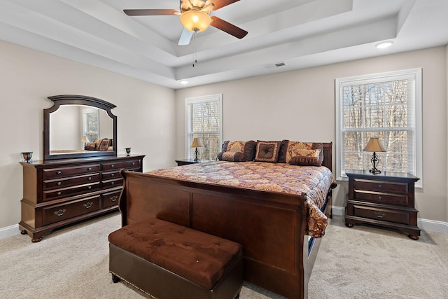 bedroom with multiple windows, ceiling fan, a raised ceiling, and light carpet