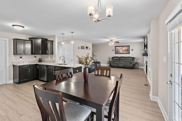 dining space with ceiling fan with notable chandelier, sink, and light wood-type flooring