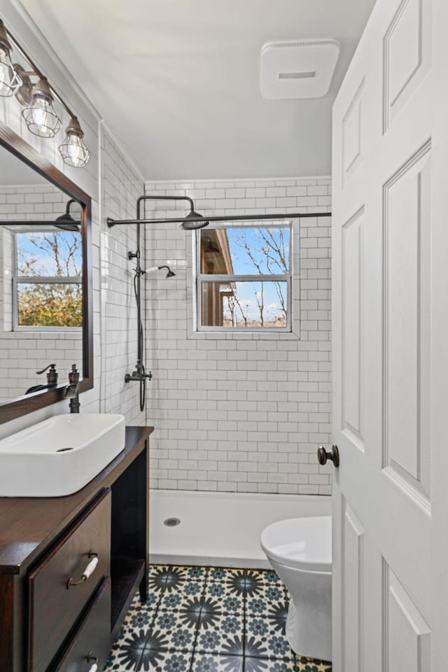 bathroom with tiled shower, vanity, and toilet