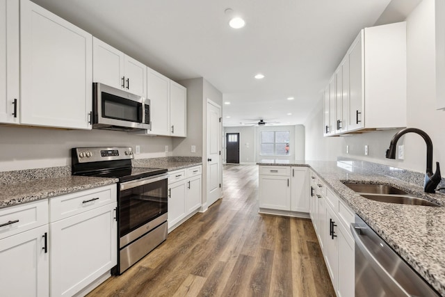 kitchen with sink, kitchen peninsula, stainless steel appliances, light stone countertops, and white cabinets