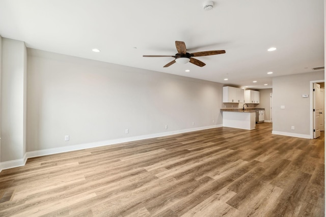 unfurnished living room with ceiling fan, sink, and light hardwood / wood-style floors