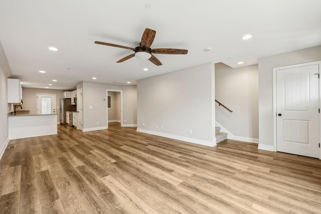 unfurnished living room with ceiling fan, sink, and light hardwood / wood-style floors