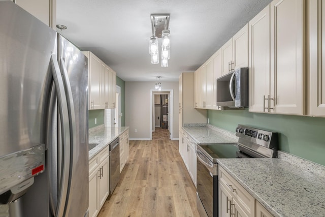 kitchen featuring pendant lighting, appliances with stainless steel finishes, light hardwood / wood-style floors, and light stone counters