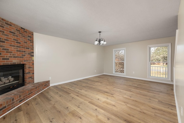 unfurnished living room featuring a brick fireplace, an inviting chandelier, a textured ceiling, and light hardwood / wood-style floors