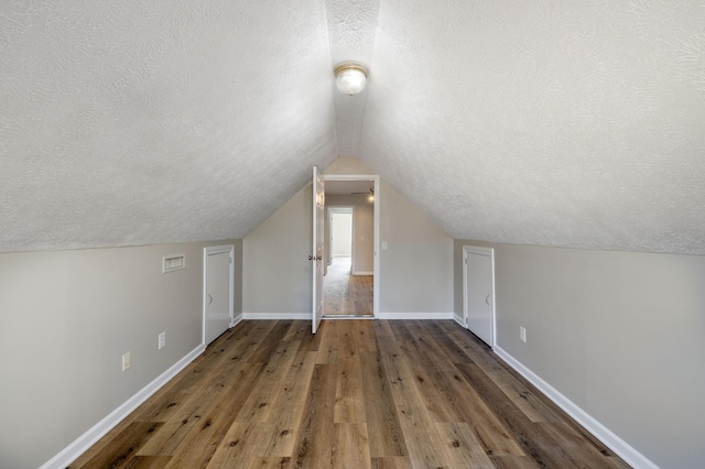 additional living space with dark wood-type flooring, a textured ceiling, and vaulted ceiling