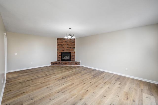 unfurnished living room with a brick fireplace, light wood-type flooring, and a chandelier