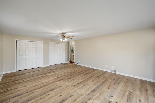 unfurnished bedroom featuring multiple closets, light hardwood / wood-style flooring, and ceiling fan