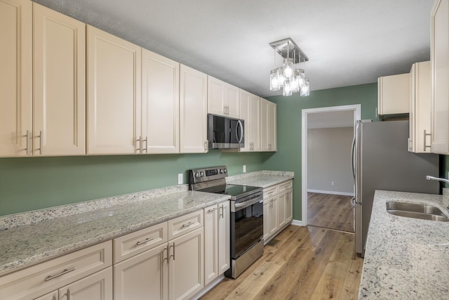 kitchen featuring sink, appliances with stainless steel finishes, pendant lighting, light stone countertops, and light hardwood / wood-style floors