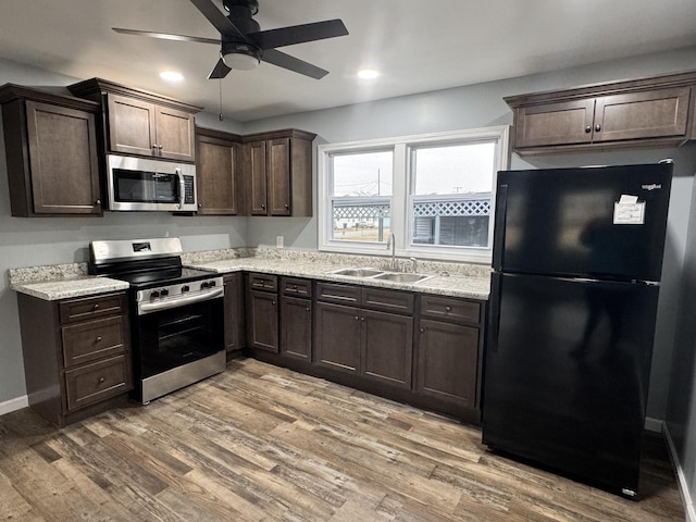 kitchen featuring sink, light hardwood / wood-style flooring, appliances with stainless steel finishes, dark brown cabinets, and light stone countertops