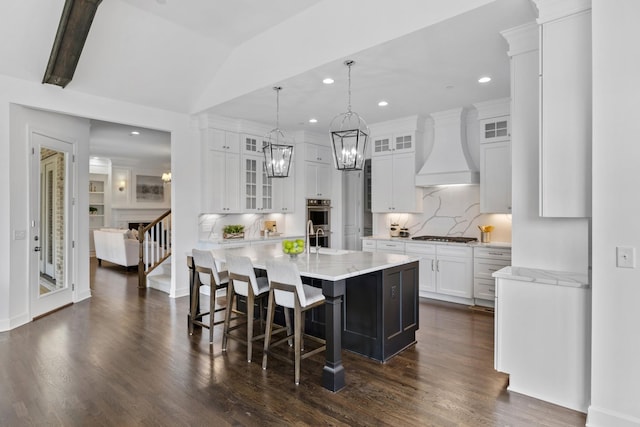 kitchen featuring a breakfast bar area, premium range hood, white cabinetry, a spacious island, and tasteful backsplash