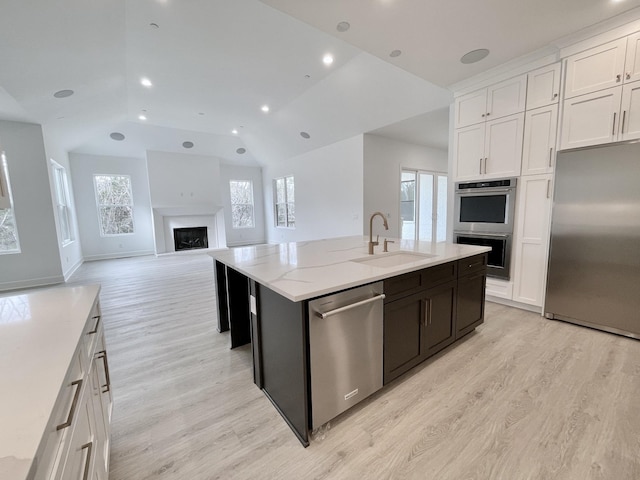 kitchen with sink, white cabinets, stainless steel appliances, light stone countertops, and a center island with sink