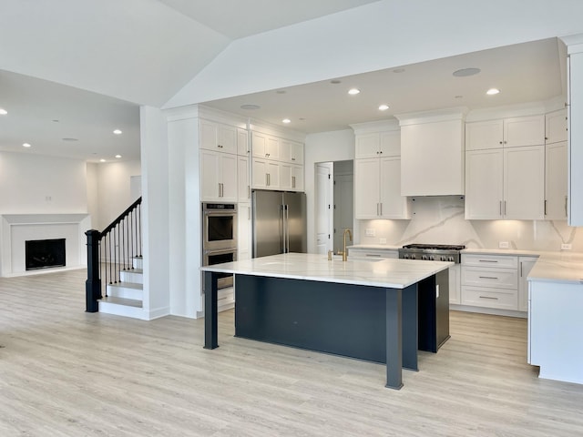 kitchen with appliances with stainless steel finishes, white cabinets, a center island with sink, vaulted ceiling, and wall chimney exhaust hood